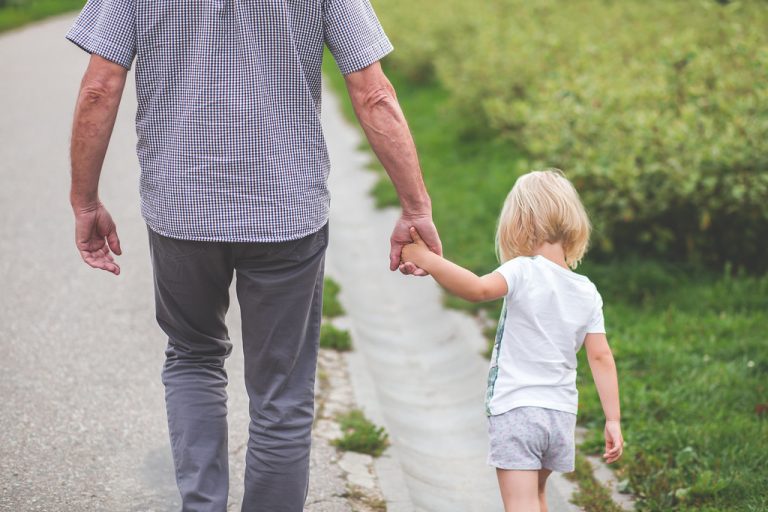 An older person's hand holding a child's while walking a path